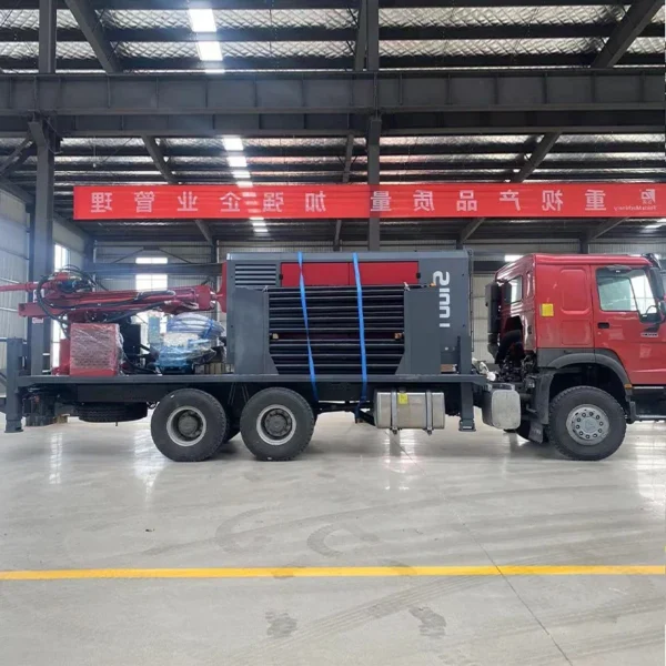 Red truck with a flatbed carrying equipment secured with straps in a warehouse setting.